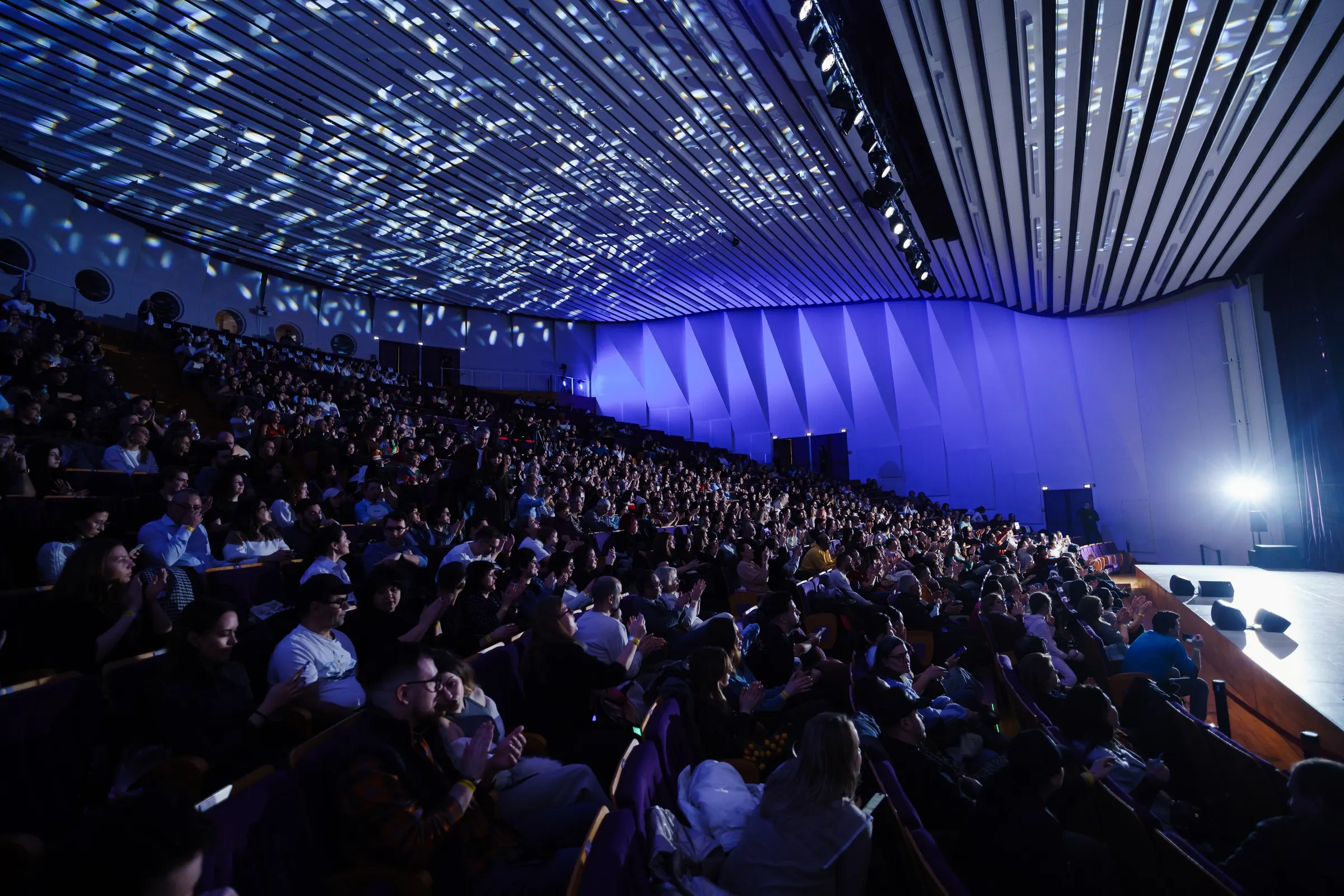 A packed venue, blue light and a ceiling lit by projections
